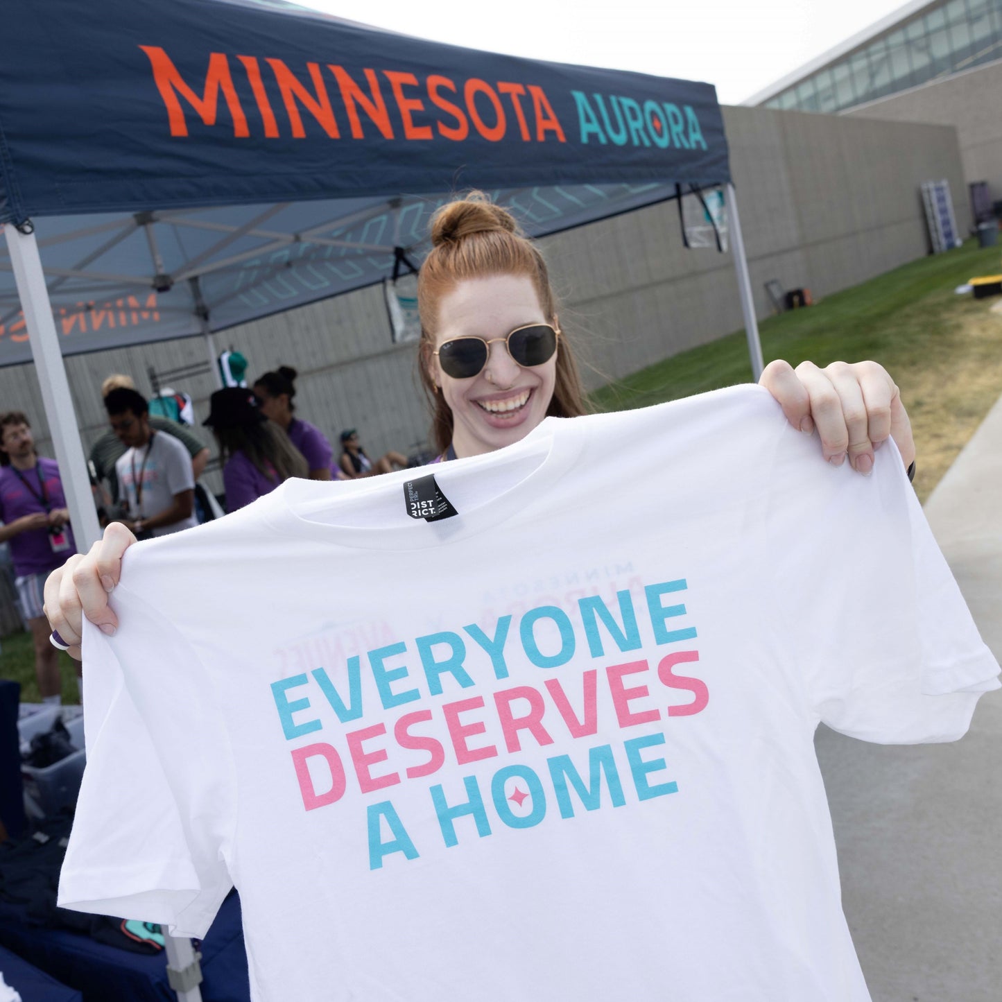 White short-sleeved shirt with the words "EVERYONE DESERVES A HOME" in light blue and pink