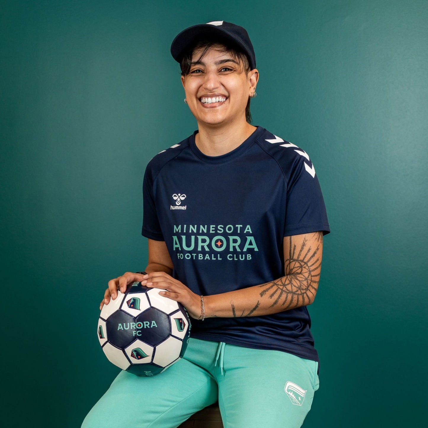 Navy blue short-sleeved shirt with the words "Minnesota Aurora Football Club" in teal and white arrows on the sholders