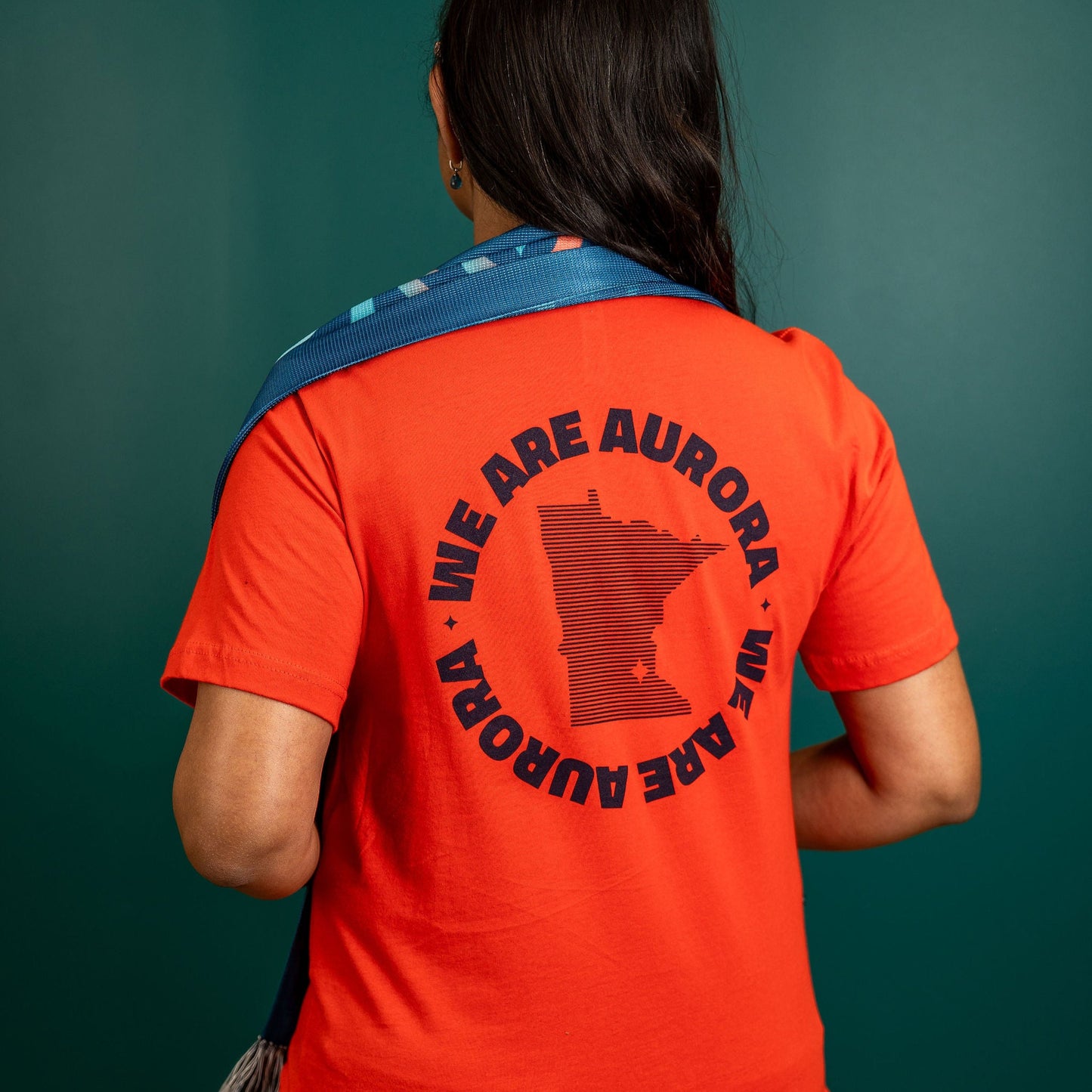 Bright red short-sleeved shirt with the state of Minnesota circled by the words "We Are Aurora"