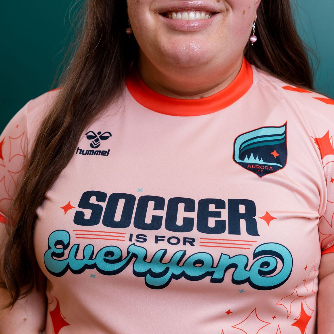 Person wearing a pink sports jersey with 'Soccer is for Everyone' text and Hummel logo.