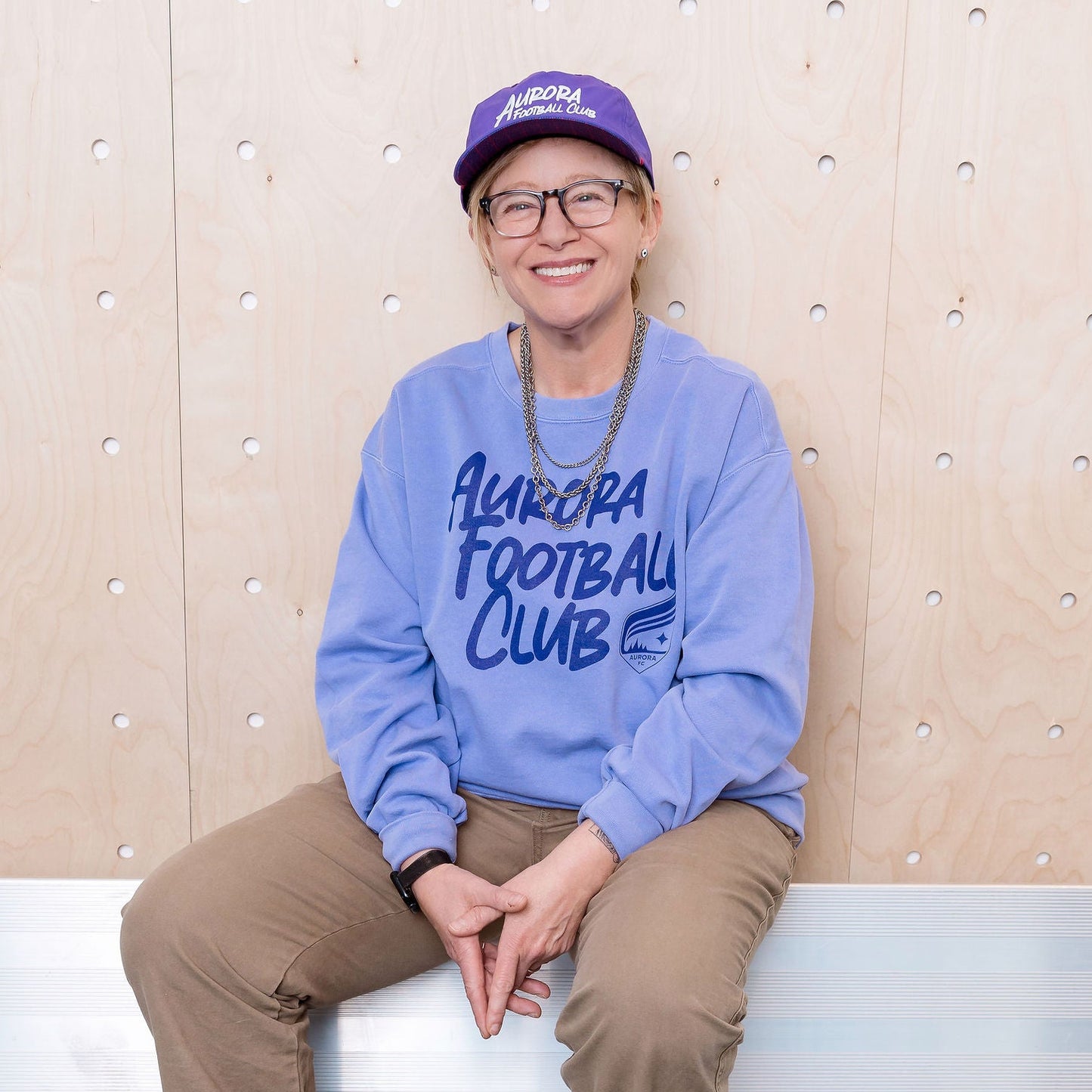 Person wearing a purple sweatshirt with text, sitting on a bench against a textured wall.