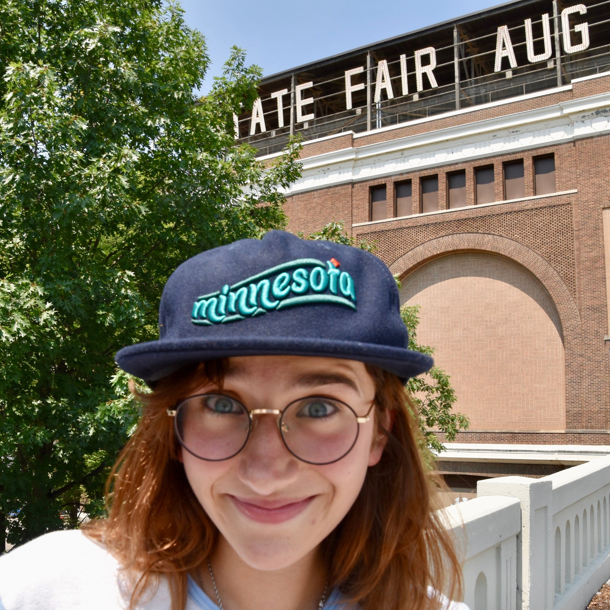 Person wearing a 'Minnesota' cap with a bridge and trees in the background