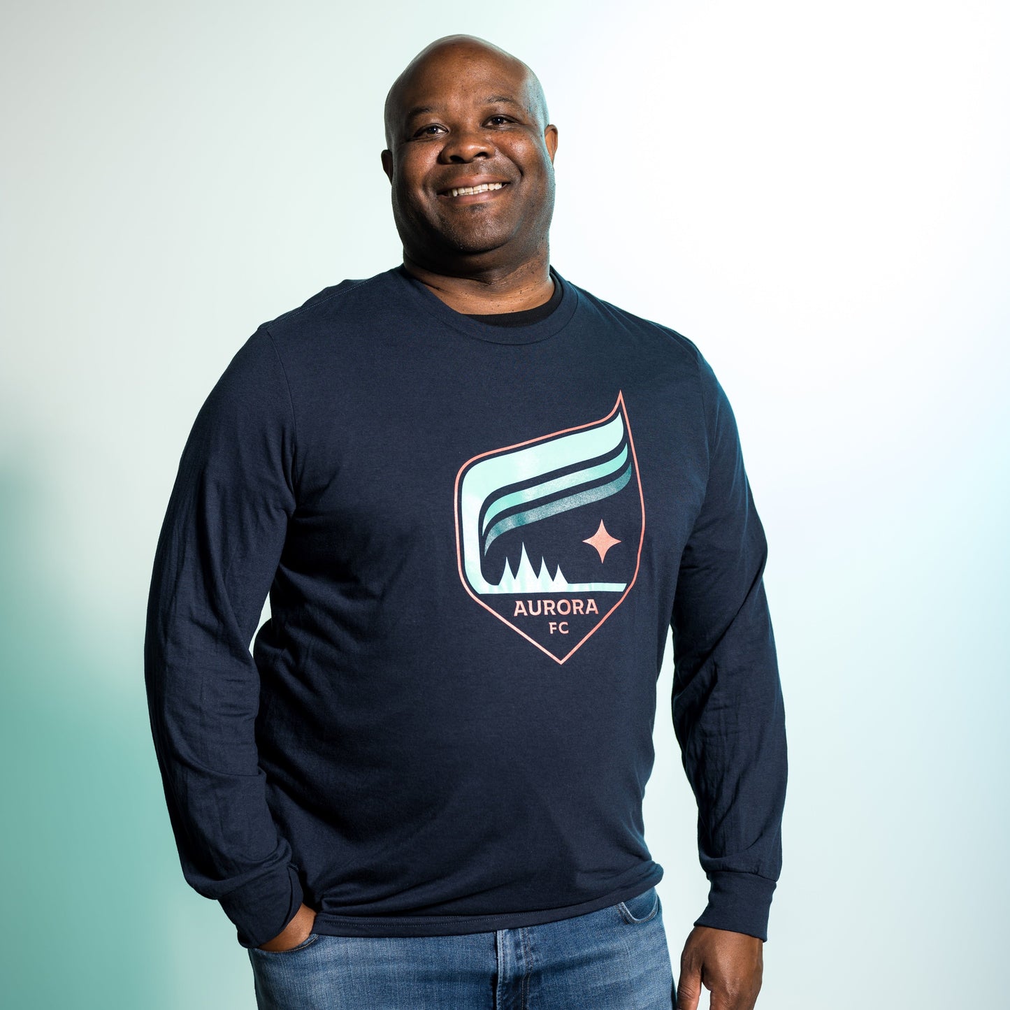 Navy blue long-sleeved shirt with the Aurora crest that features the colors teal and orange