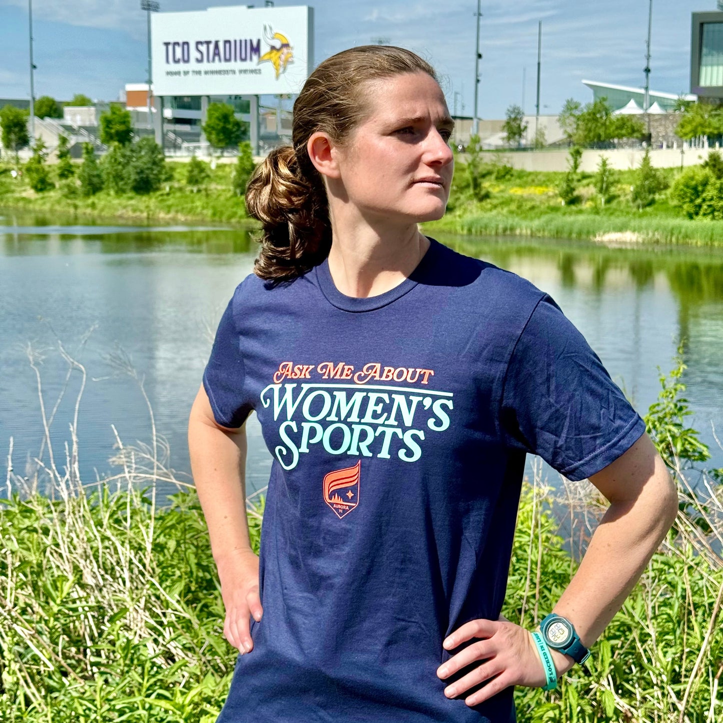 Navy blue short-sleeved shirt with the words "Ask Me About Women's Sports" and the Aurora Crest