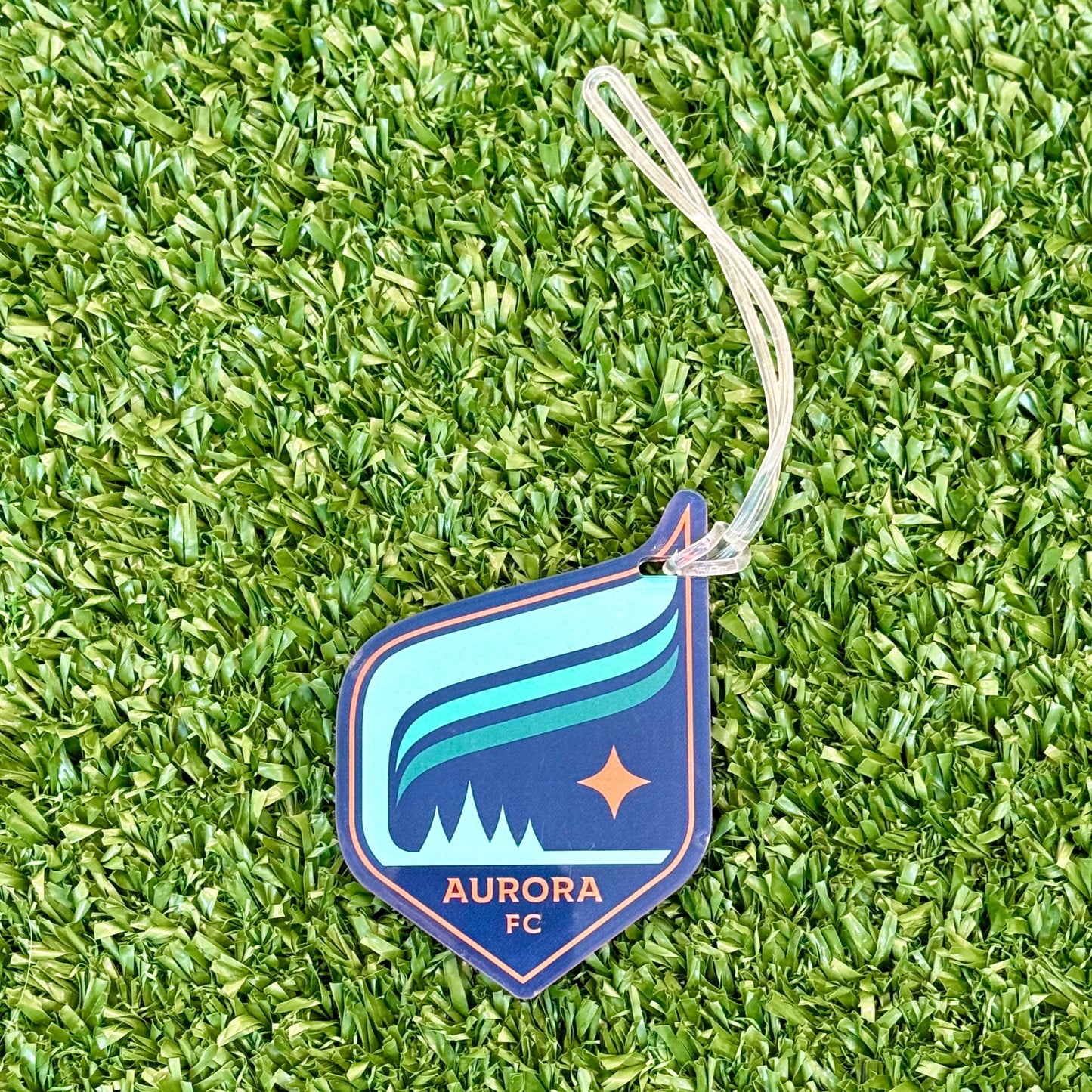 Plastic luggage tag with a clear string attached featuring the Aurora crest