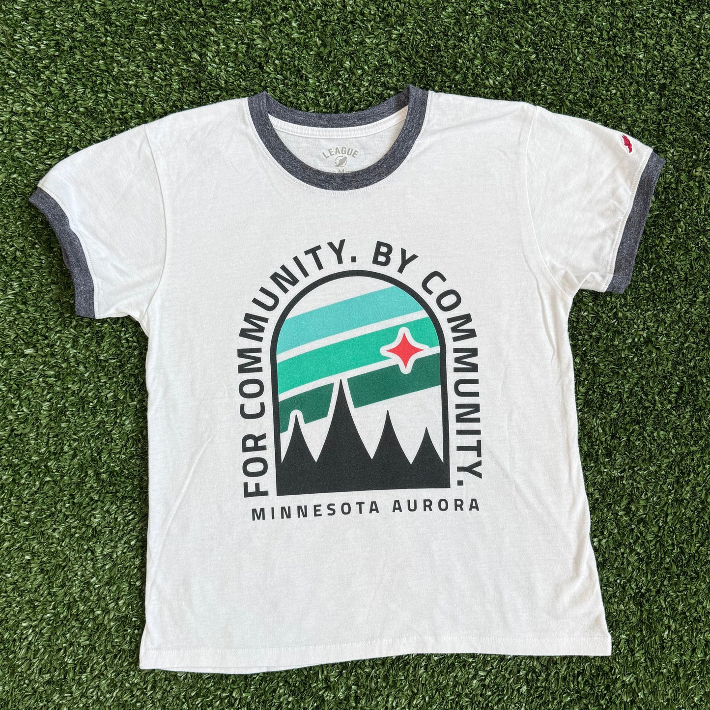 White t-shirt with a logo and text on a green grass-like surface