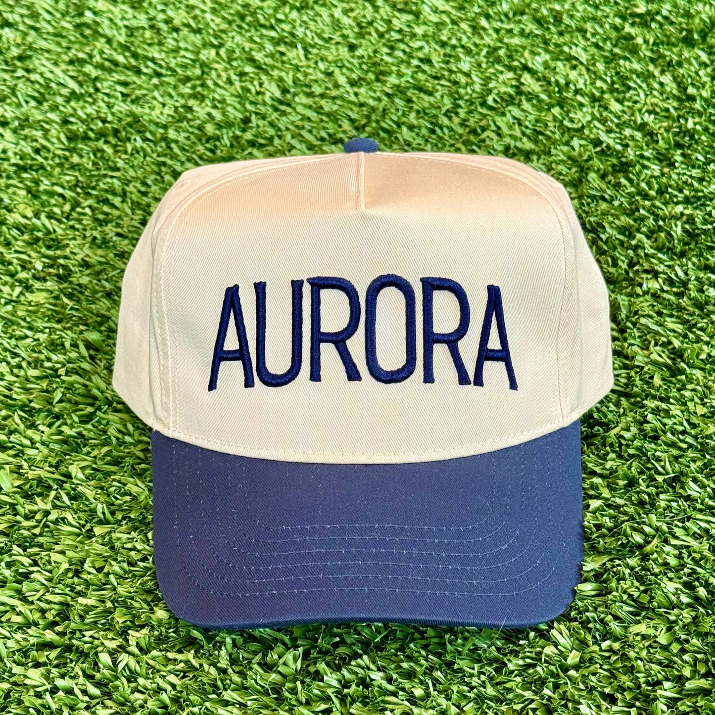 Trucker hat with navy 'AURORA' on a green grass background