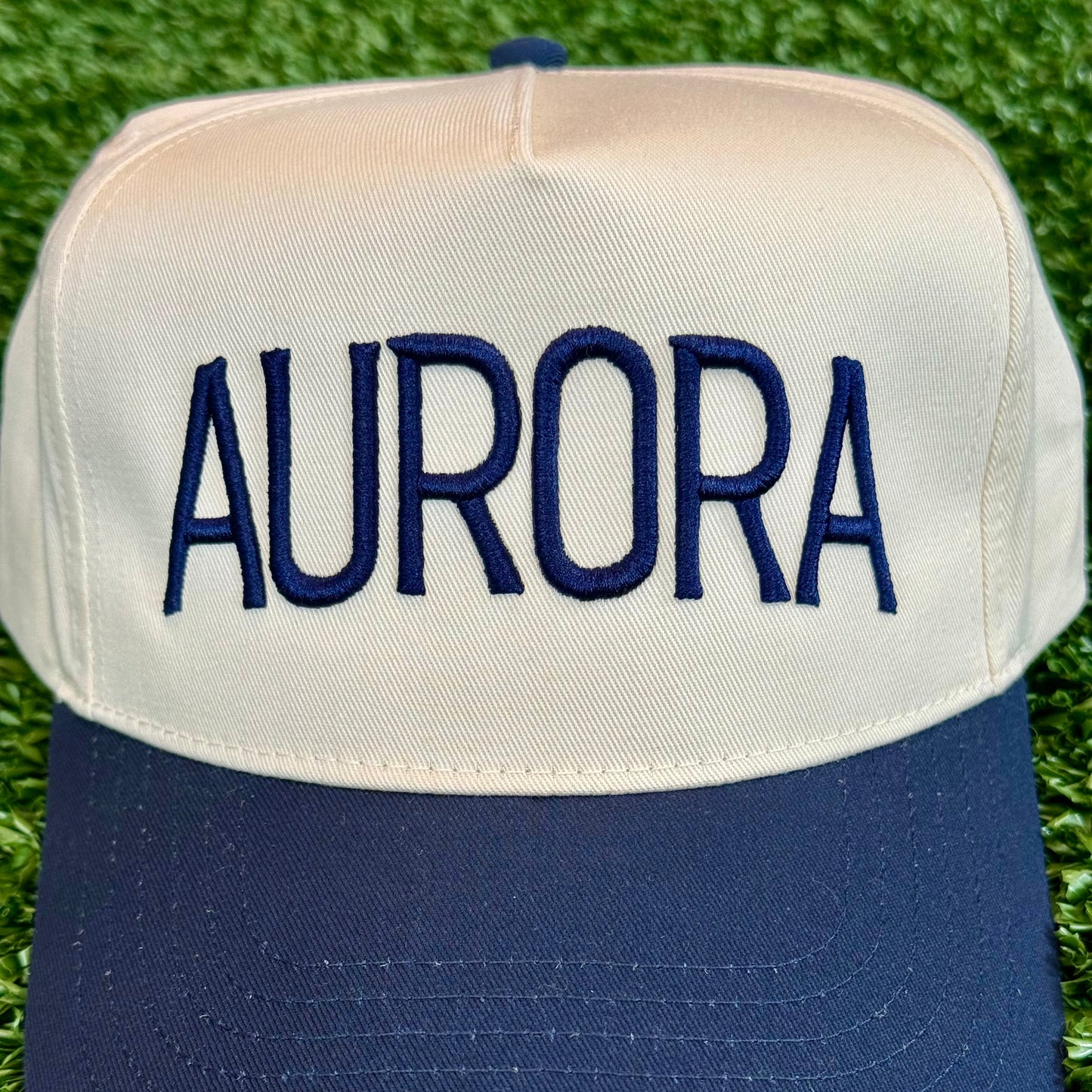 close up of embroidered Cap with 'AURORA' embroidered on it, placed on grass.