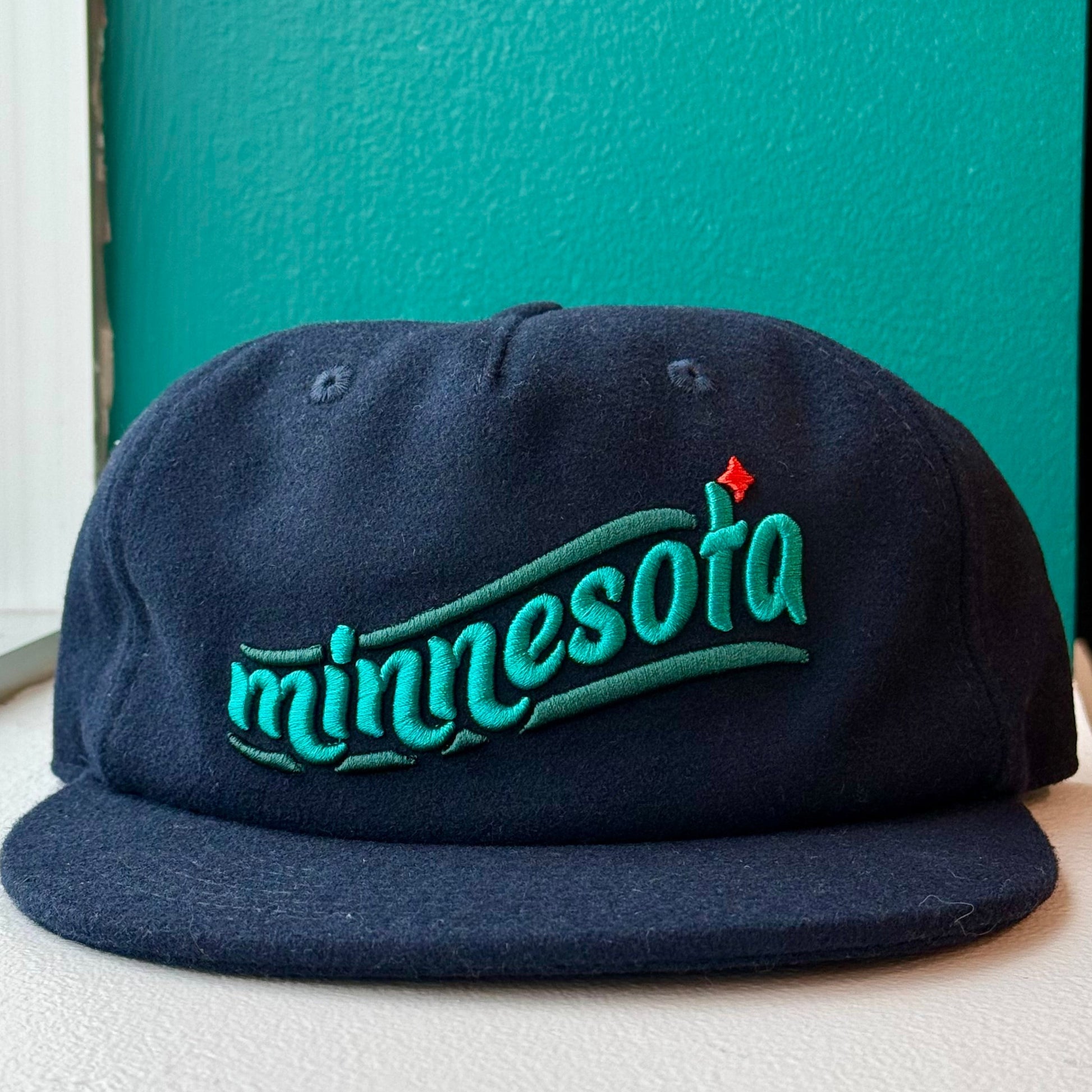 Navy blue cap with 'Minnesota' text on a surface near a window with a teal wall.