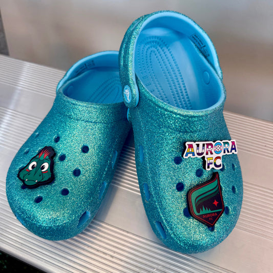 Blue glittery crocs with jibbitz charms on a bench surface