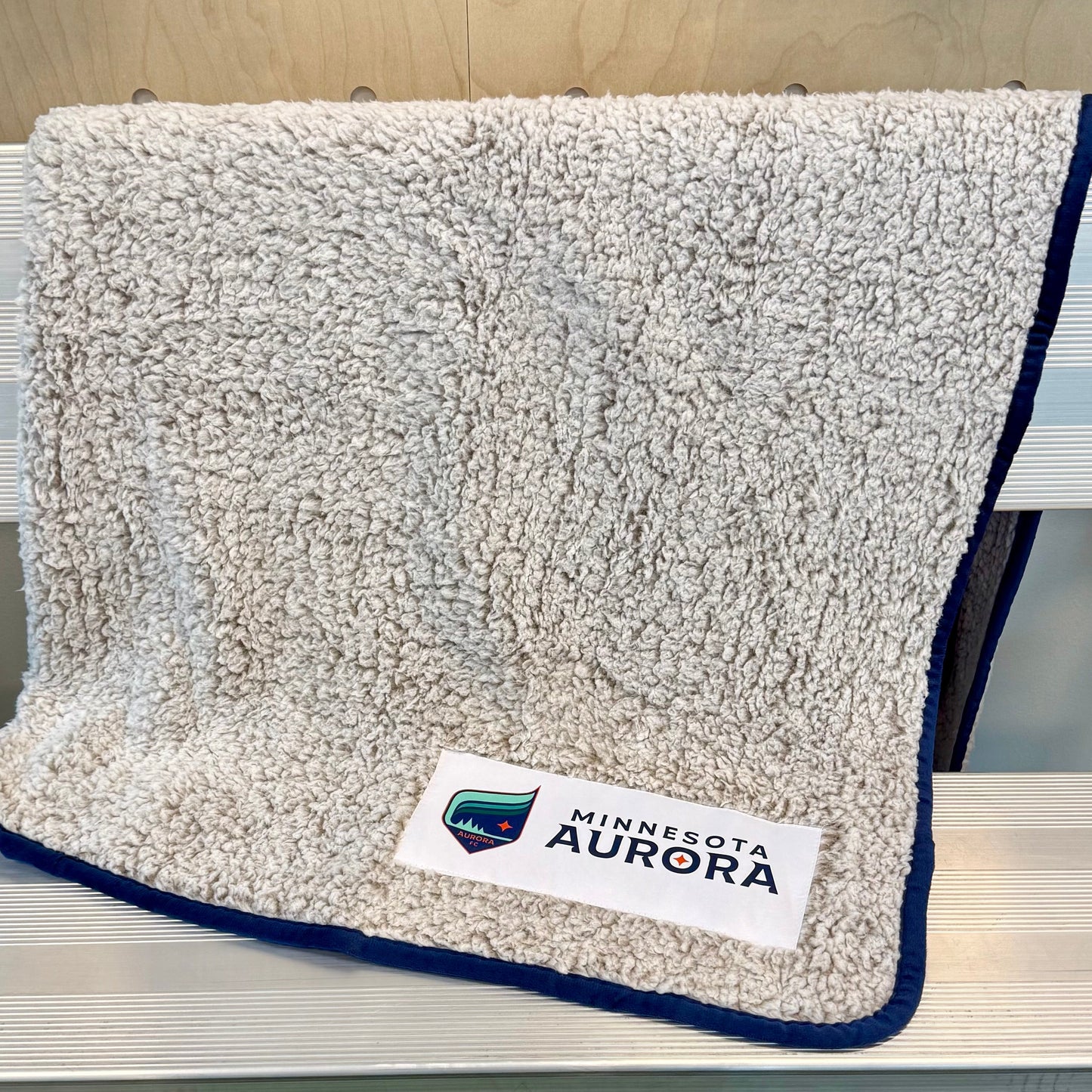 Gray blanket with a logo on a metal bench against a wooden wall.