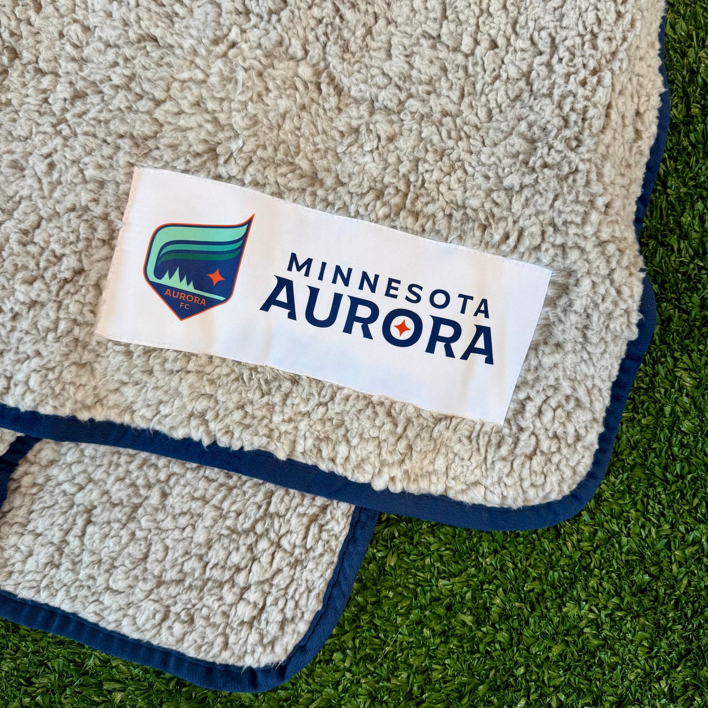Grey blanket with 'Minnesota Aurora' label on a grass background