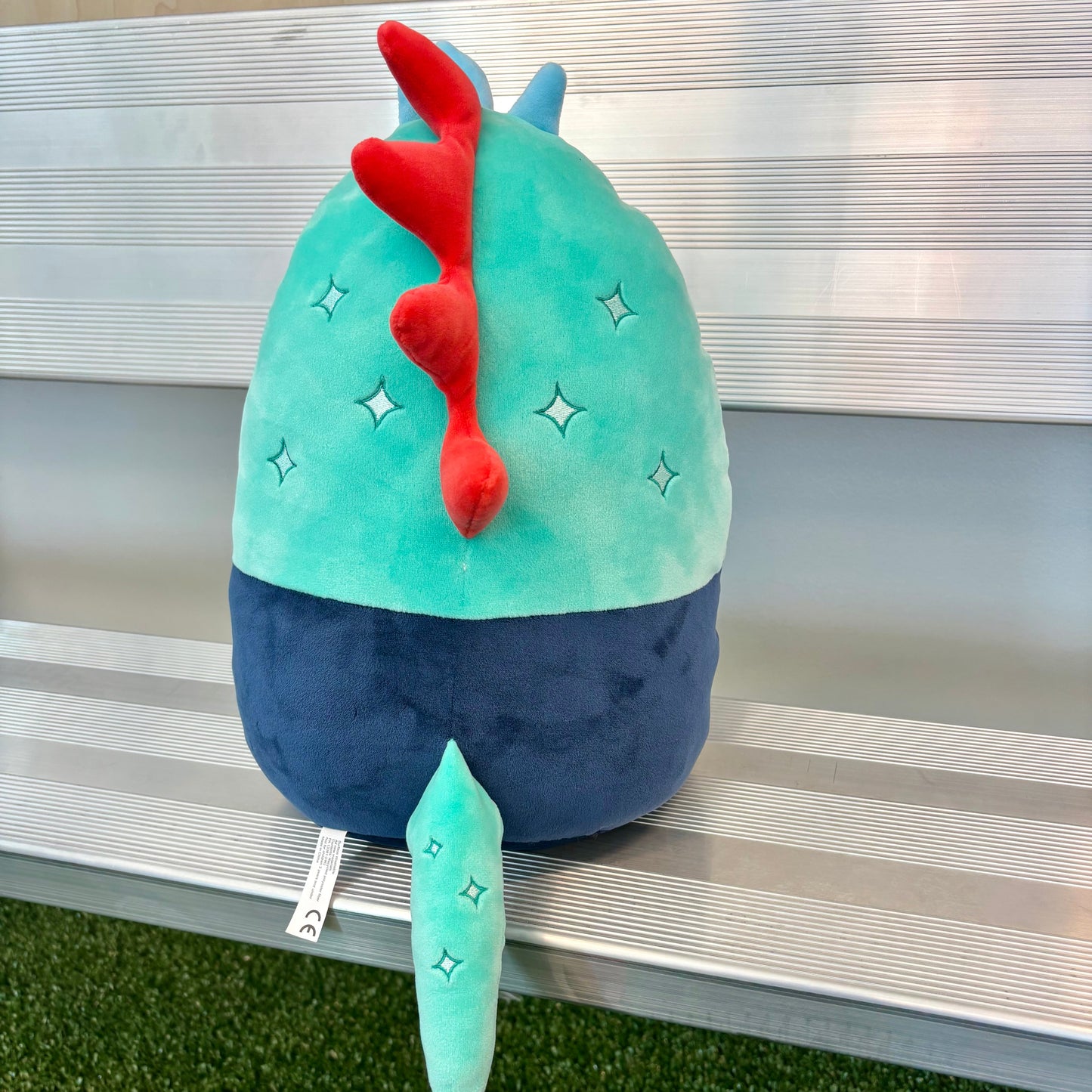 Plush toy with a green body, red accents, and star-shaped feet on a metallic surface.