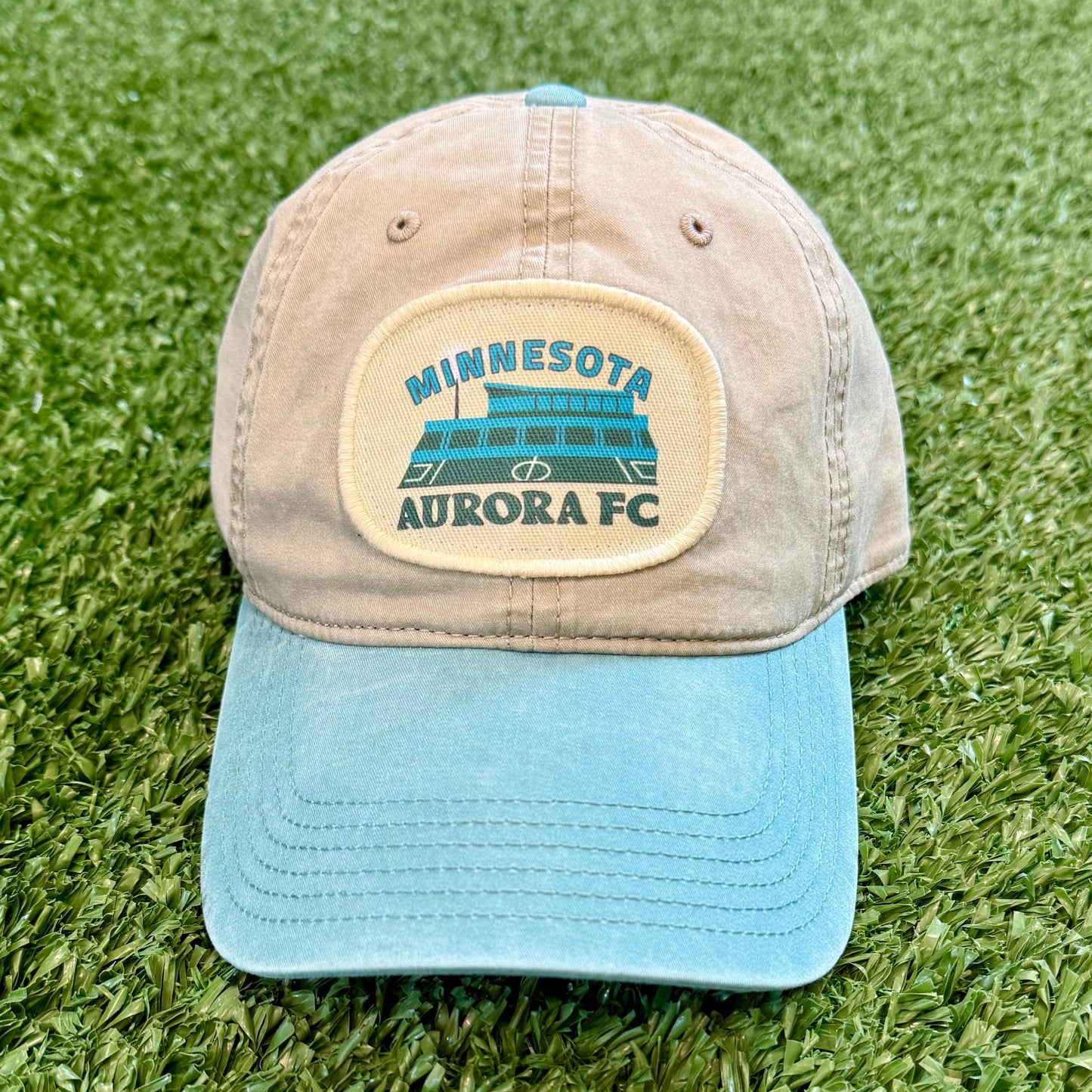 Cap with Minnesota Aurora FC logo on a grassy surface