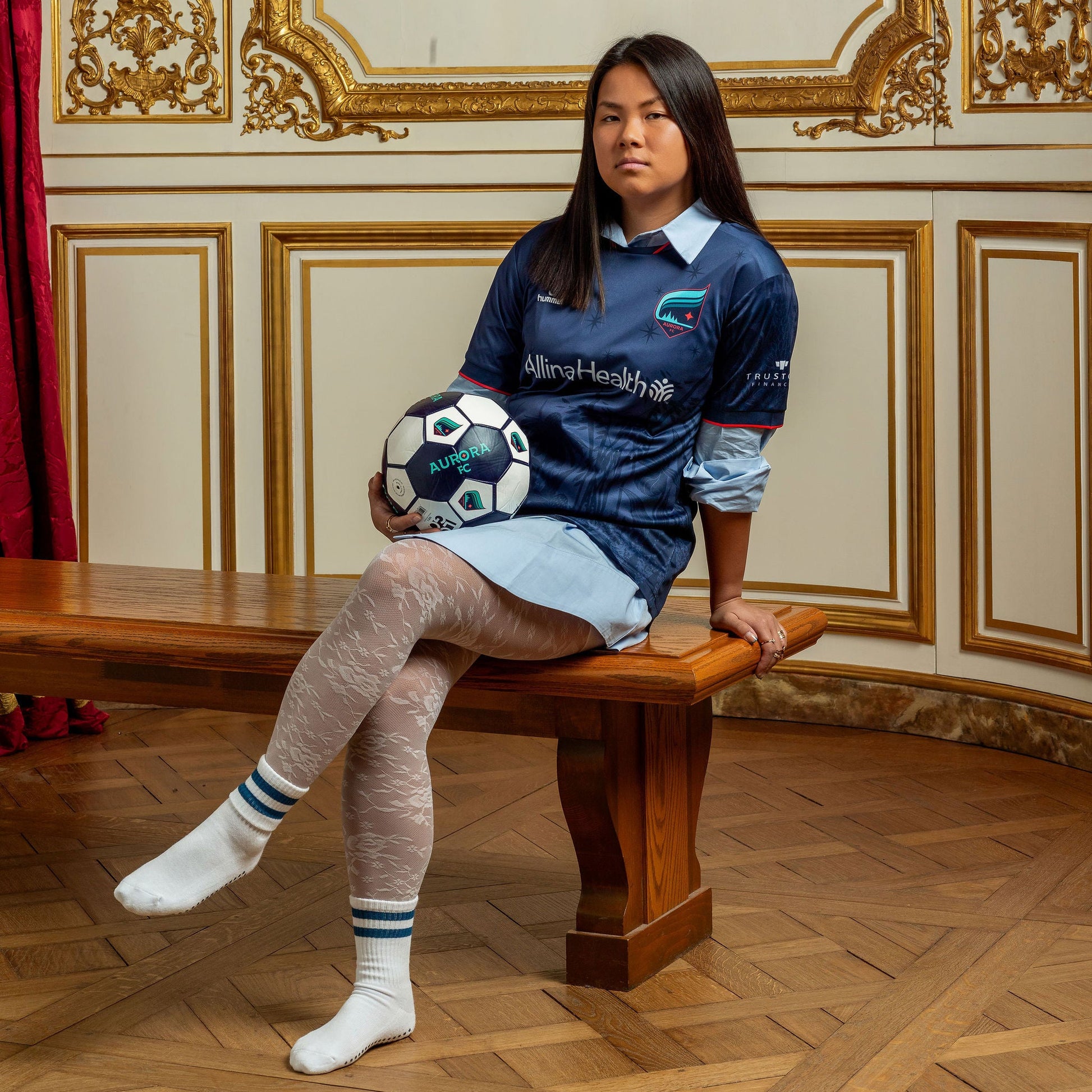 Woman sitting on a bench holding a soccer ball in an ornate room