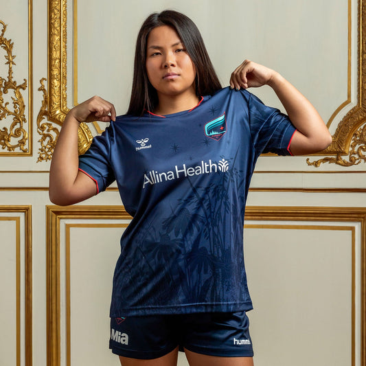 Person wearing a navy jersey with 'Allina Health' branding in an ornate room.