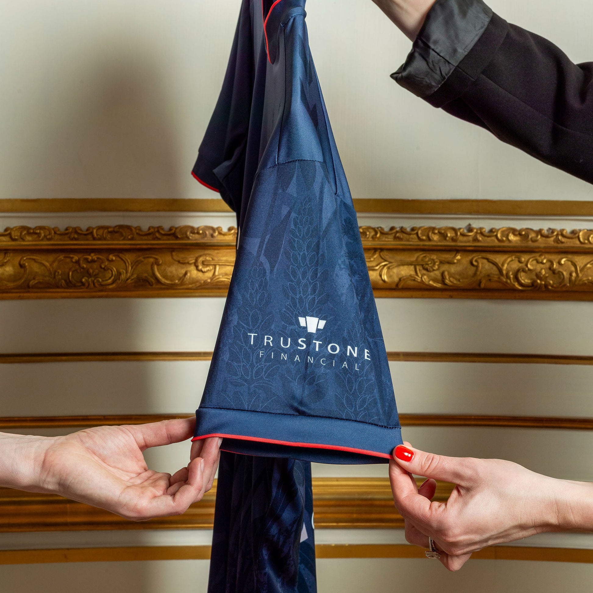 Navy blue jersey with TruStone Financial logo held by two hands against a decorative wall.