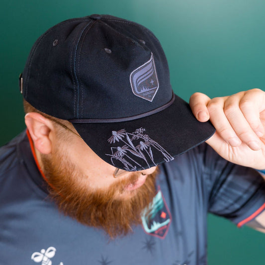 Person wearing a navy cap with a logo, adjusting it against a green background