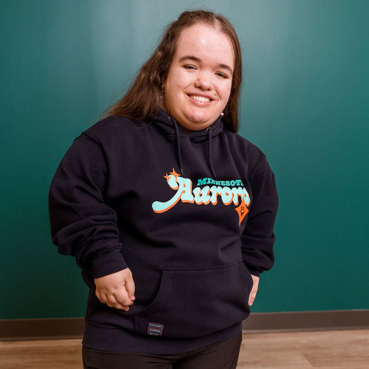 Person wearing a navy hoodie with colorful text against a teal wall.