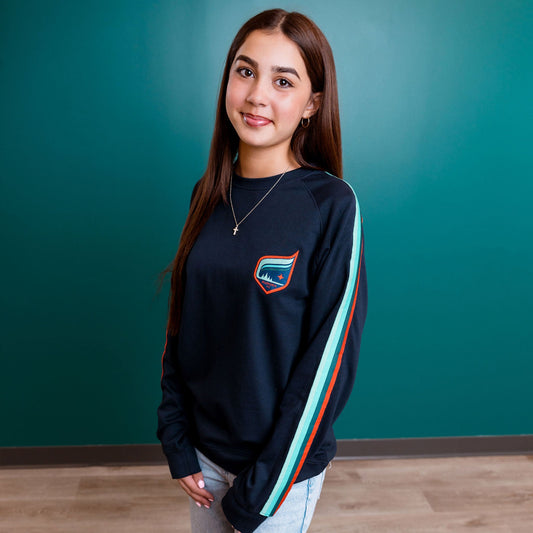 Woman wearing a navy sweatshirt with a logo against a teal wall.