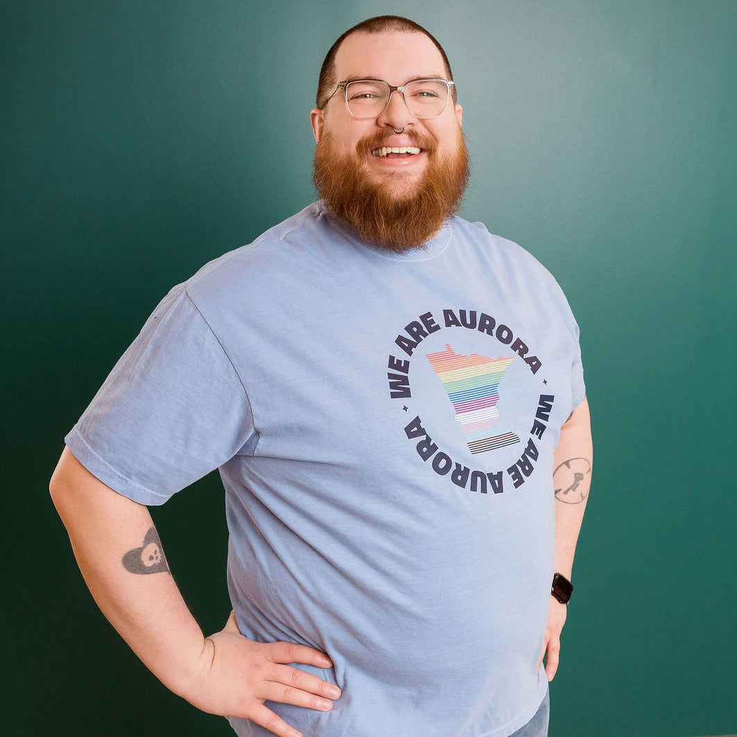 Man wearing a blue t-shirt with a rainbow design and text, standing in front of a green wall.