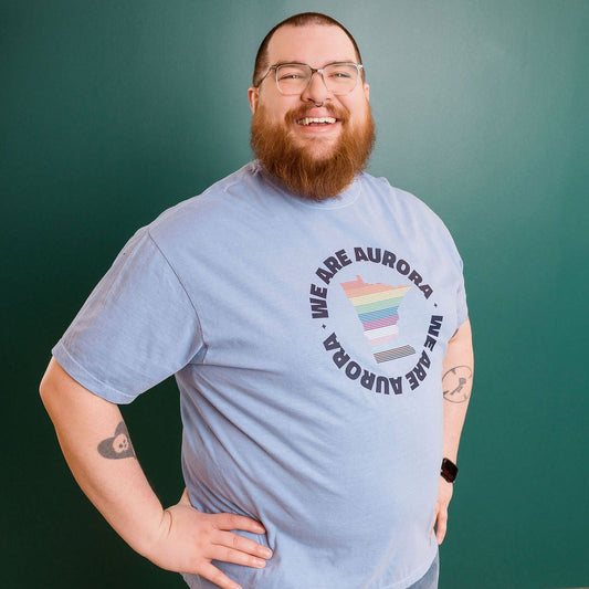 Man wearing a blue t-shirt with a rainbow design and text, standing in front of a green wall.