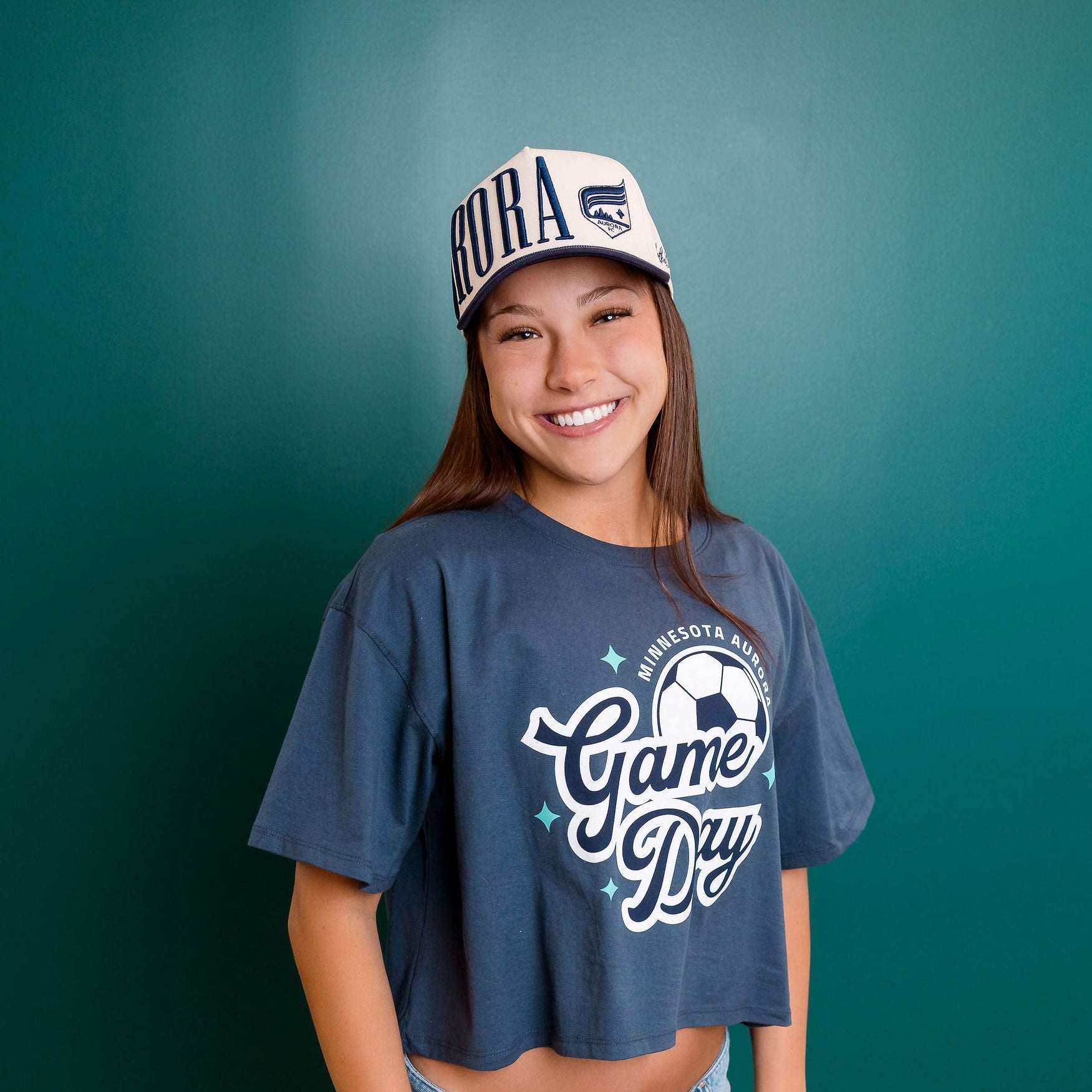 Person wearing a navy blue t-shirt with 'Game Day' text and a cap, standing against a teal wall.