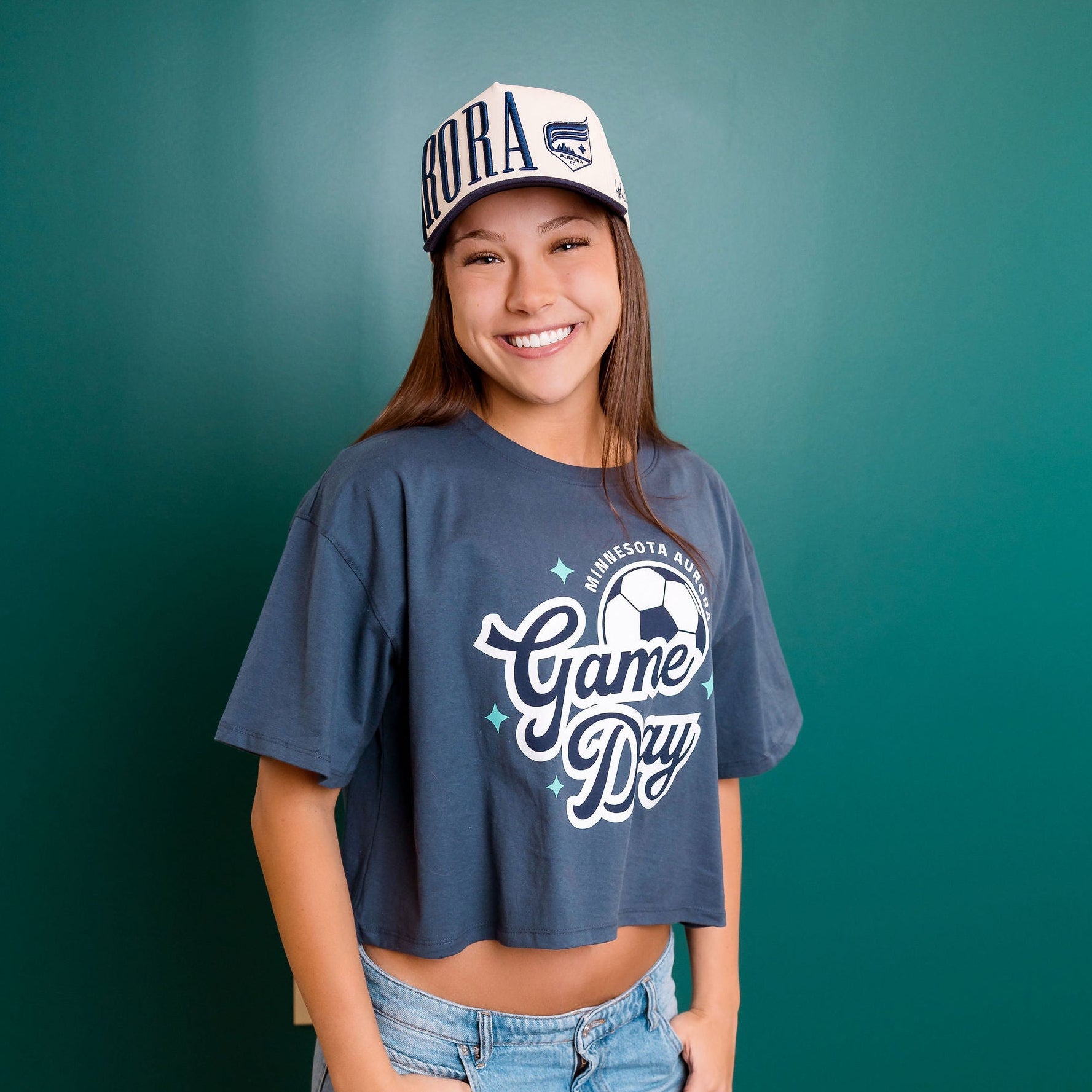 Person wearing a 'Game Day' t-shirt and cap against a teal wall