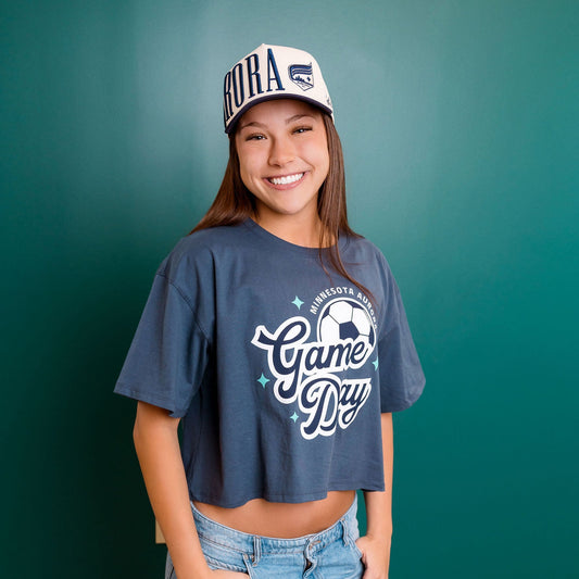 Person wearing a 'Game Day' t-shirt and cap against a teal wall