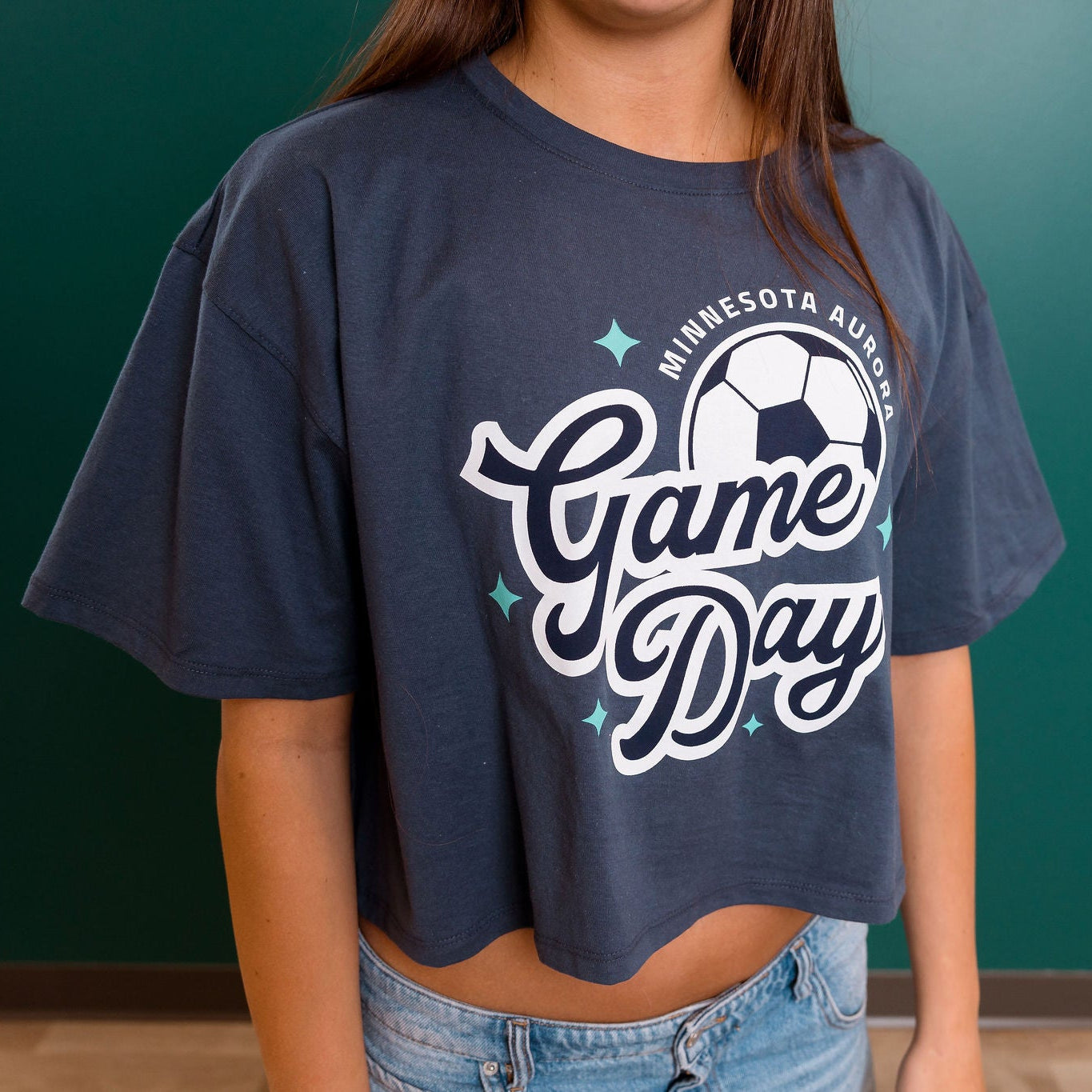 Person wearing a navy blue 'Game Day' t-shirt with a soccer ball graphic against a green wall.
