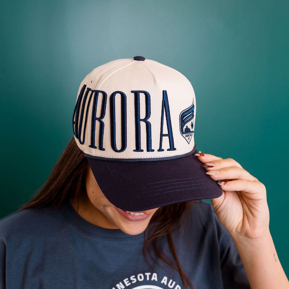Person wearing a cap with 'Aurora' text against a teal background