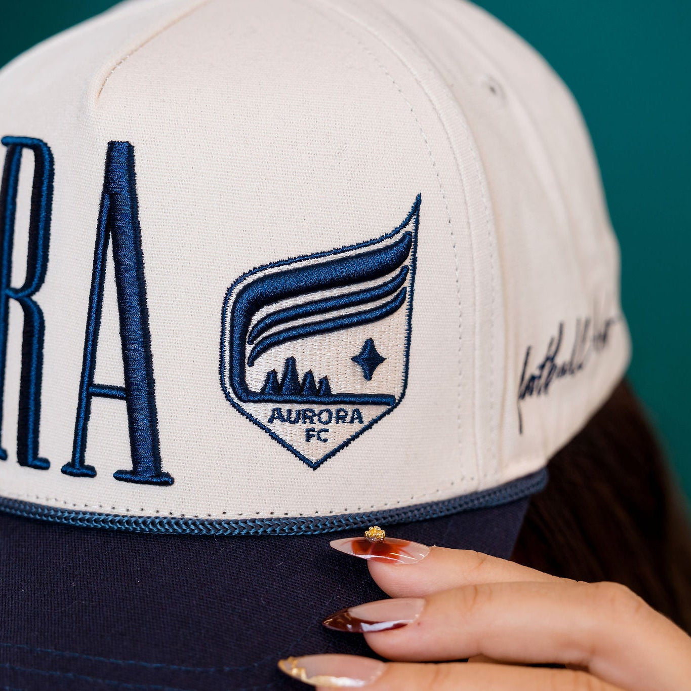 Close-up of a cap with 'Aurora FC' branding on a blurred background