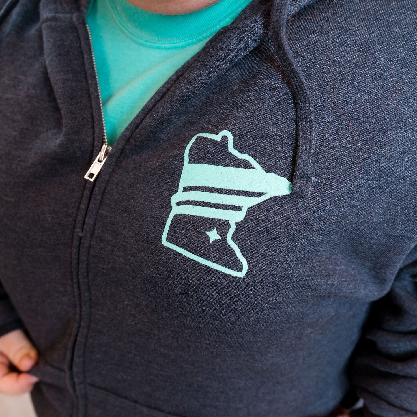 Person wearing a dark hoodie with a light blue logo on a neutral background