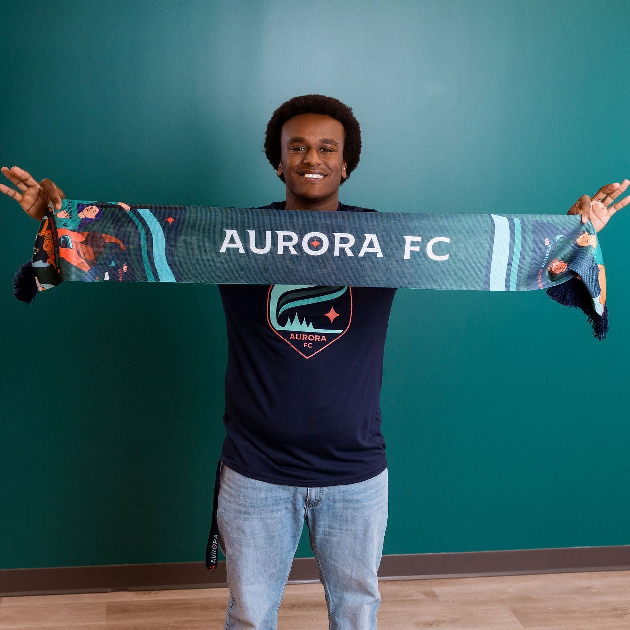 Person holding an Aurora FC scarf against a teal background