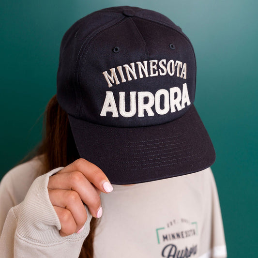 Navy cap with 'Minnesota Aurora' text held by a person against a green background