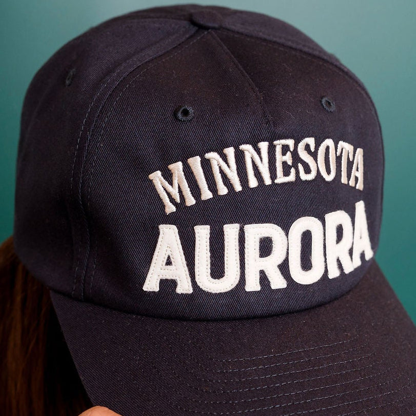 Person wearing a navy cap with 'Minnesota Aurora' text on a green background
