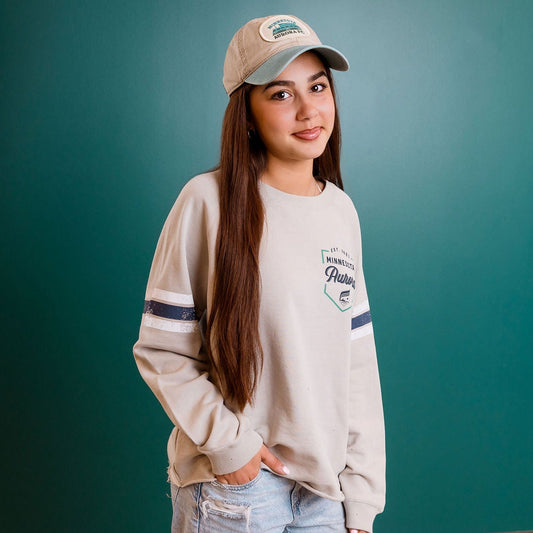 Person wearing a beige sweatshirt and cap standing against a teal wall.