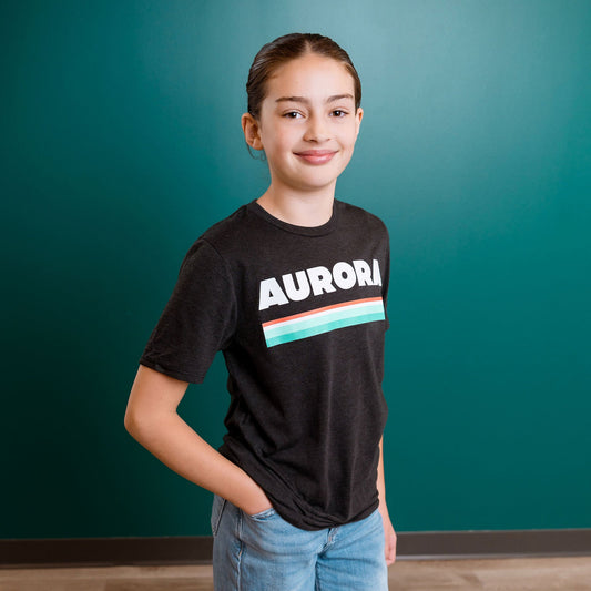 Person wearing a black t-shirt with 'Aurora' printed on it against a teal wall.