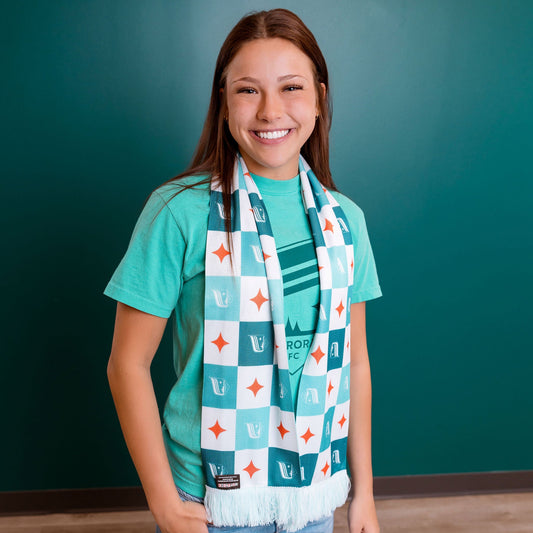 Person wearing a teal shirt and patterned scarf against a teal wall.