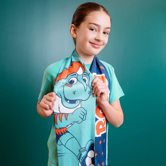 Child wearing a colorful scarf with a Rory mascot design against a teal wall.