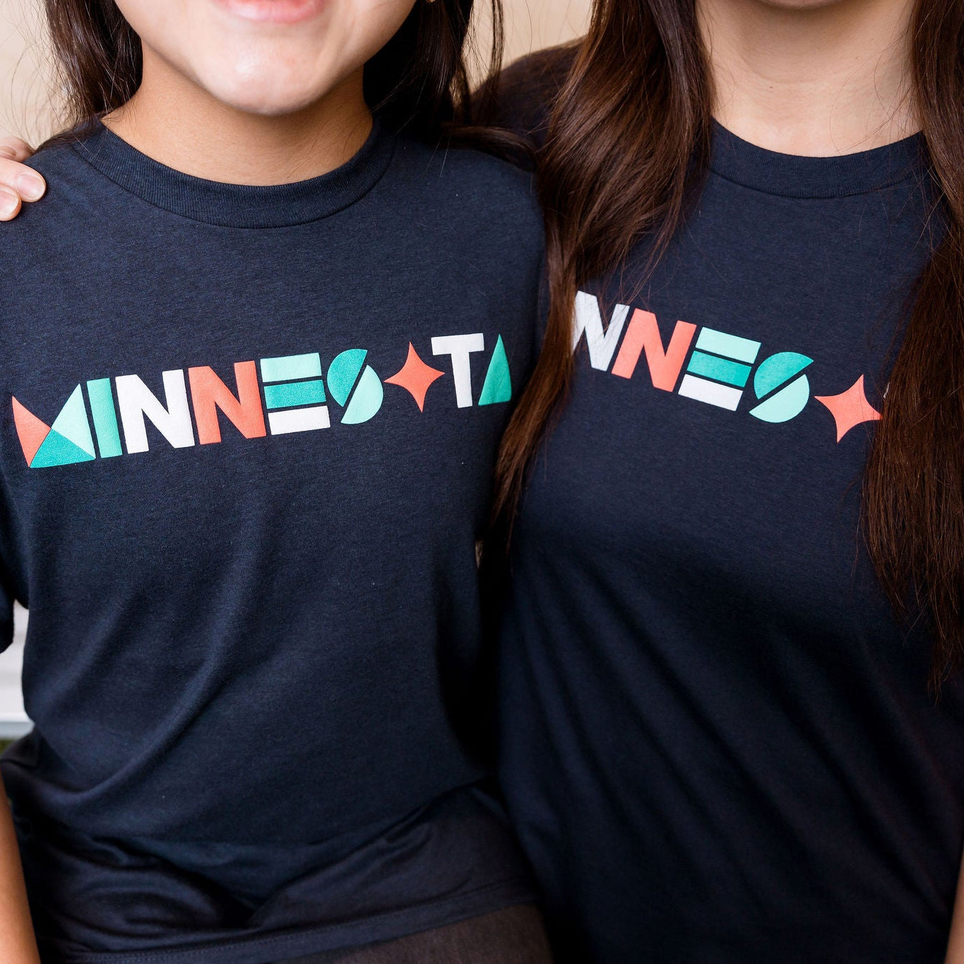 Two people wearing navy blue t-shirts with colorful 'MINNESOTA' text.