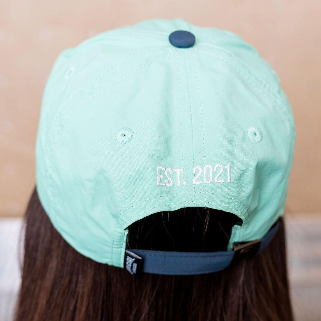 Light teal cap with 'EST 2021' text worn by a person, blurred background