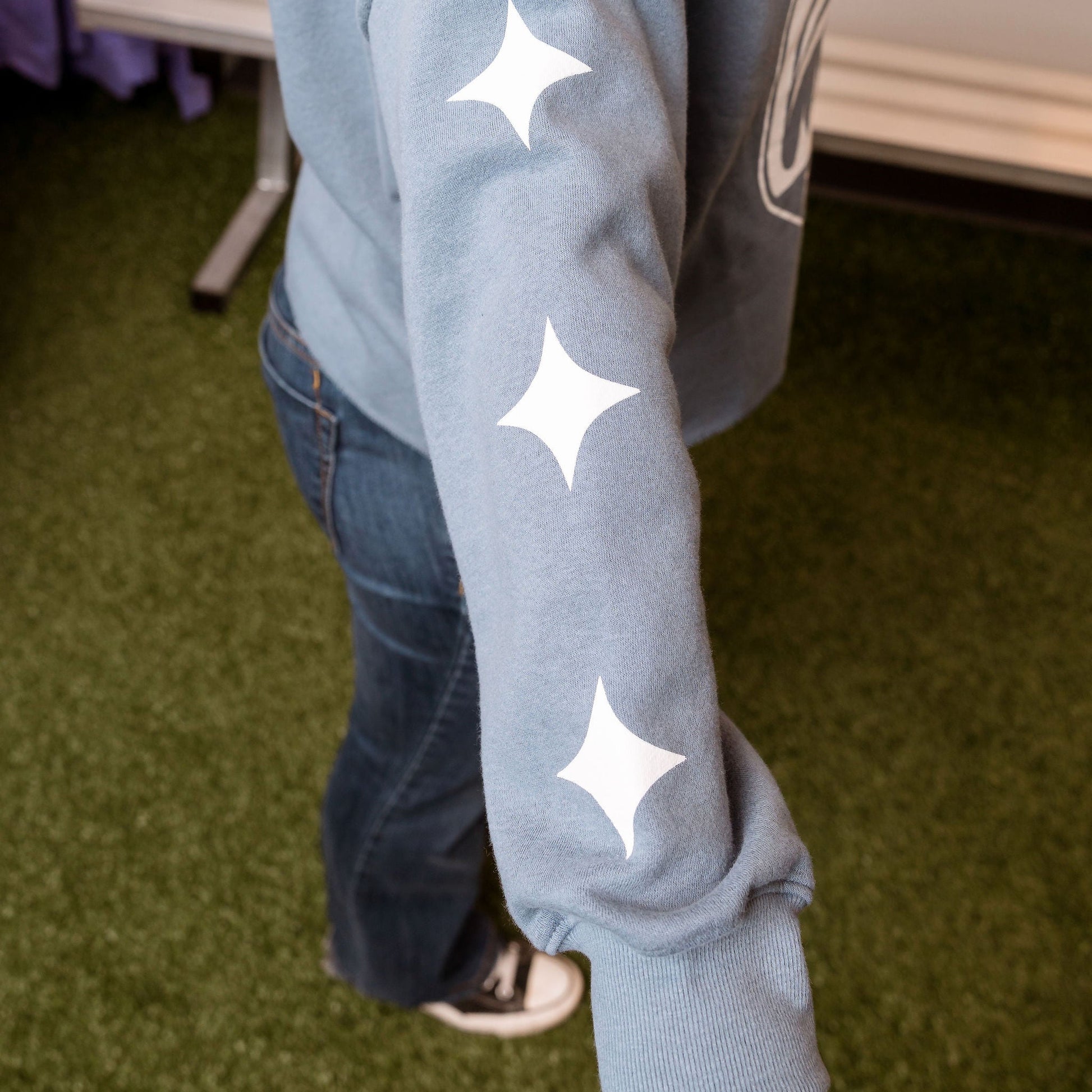 Person wearing a light blue hoodie with white star patterns on a green floor.
