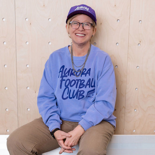 Person wearing a purple sweatshirt with text, sitting on a bench against a wooden paneled wall.