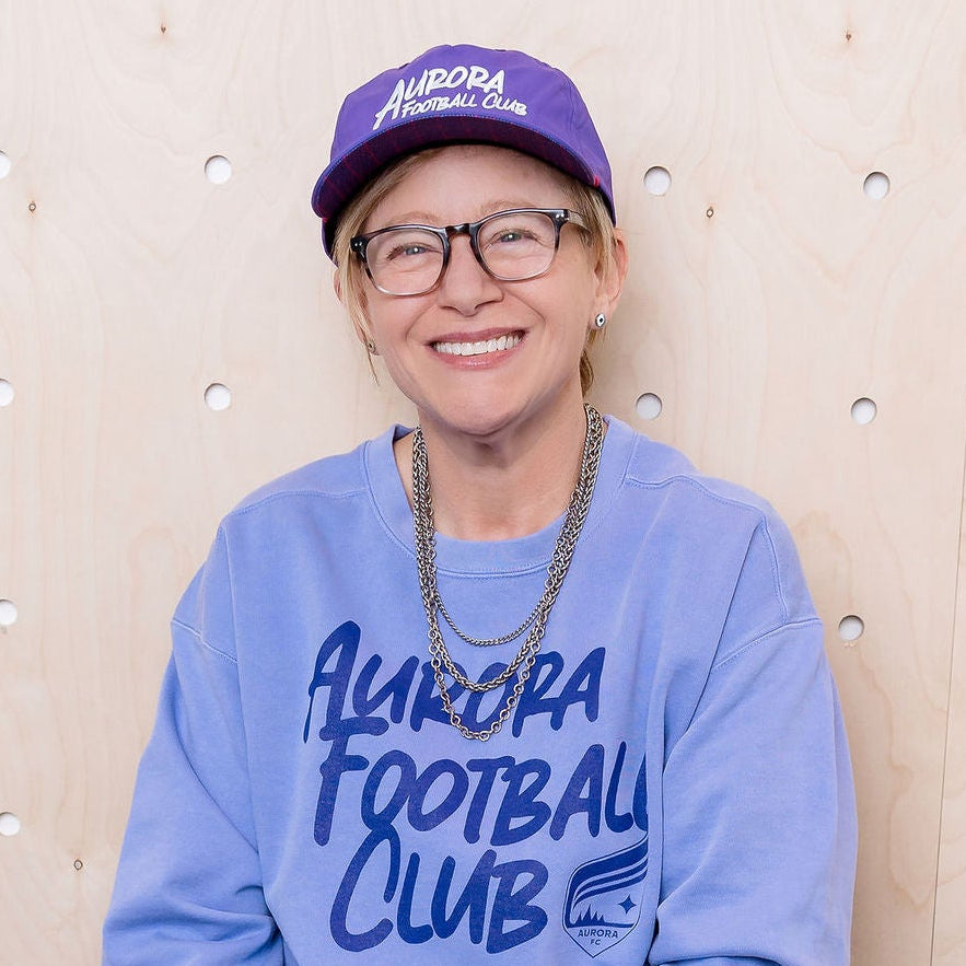 Person wearing a purple sweatshirt with text, sitting on a bench against a textured wall.