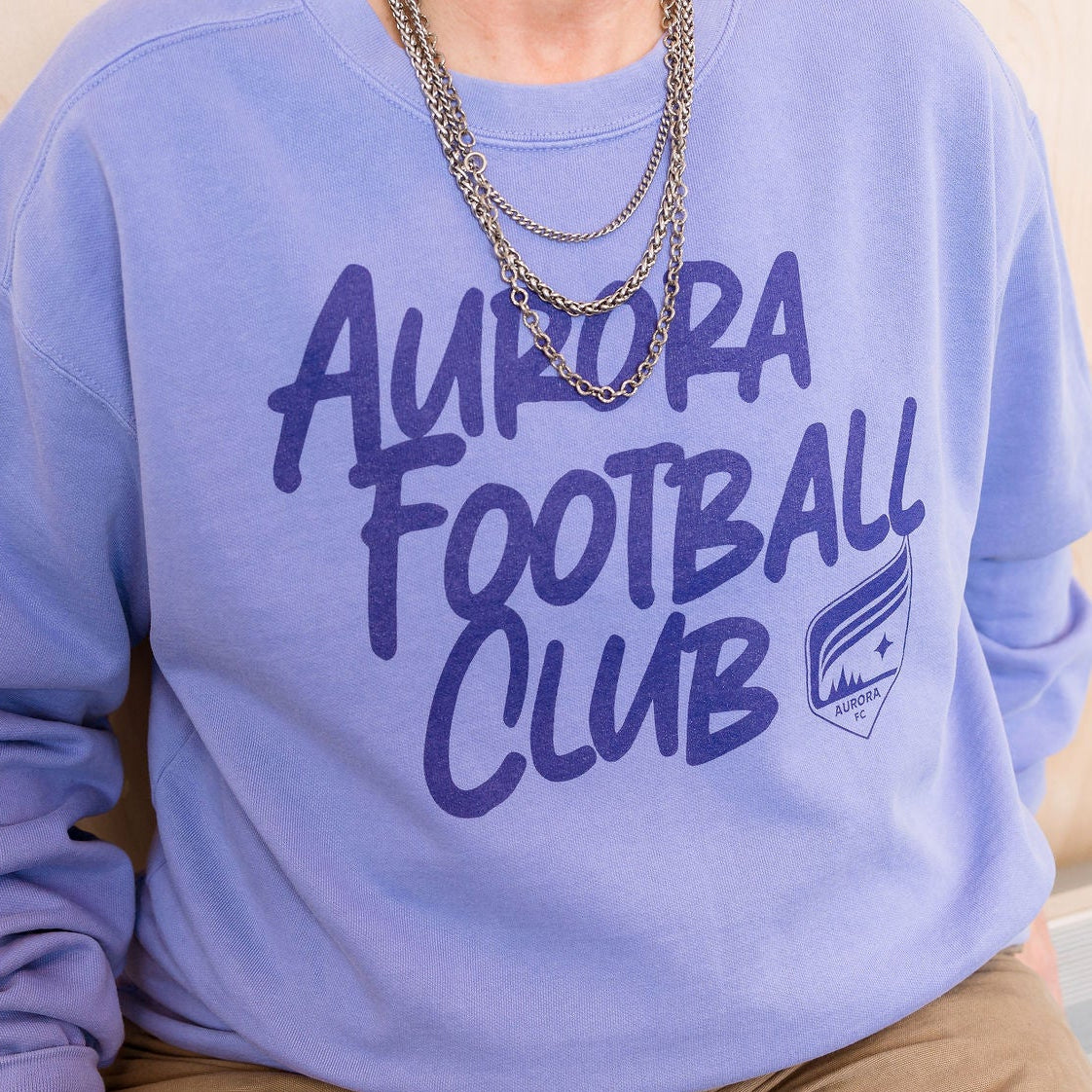 Person wearing a purple 'Aurora Football Club' sweatshirt in an indoor setting.