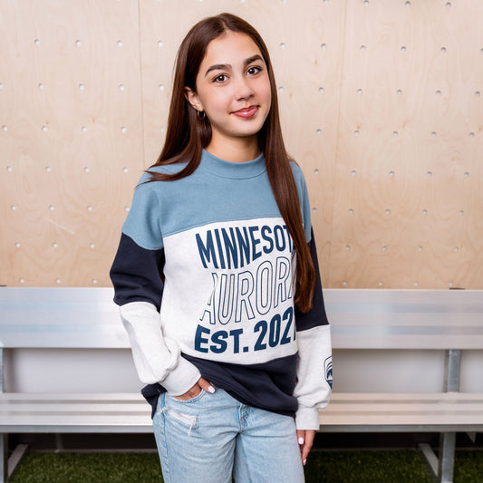 Person wearing a Minnesota Aurora sweatshirt and jeans standing in a casual setting.