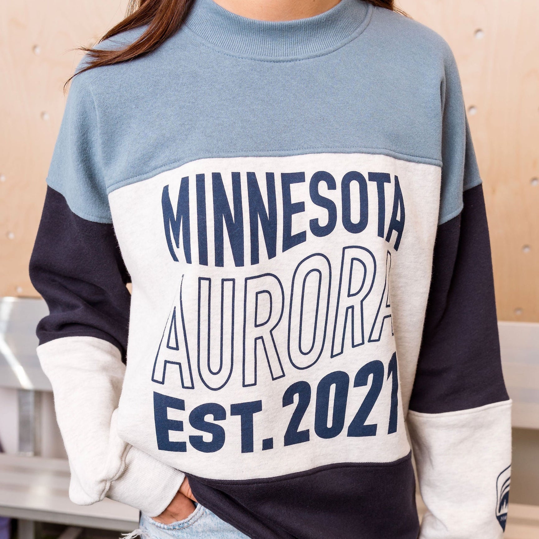 Person wearing a sweatshirt with 'Minnesota Aurora EST. 2021' text, standing indoors.