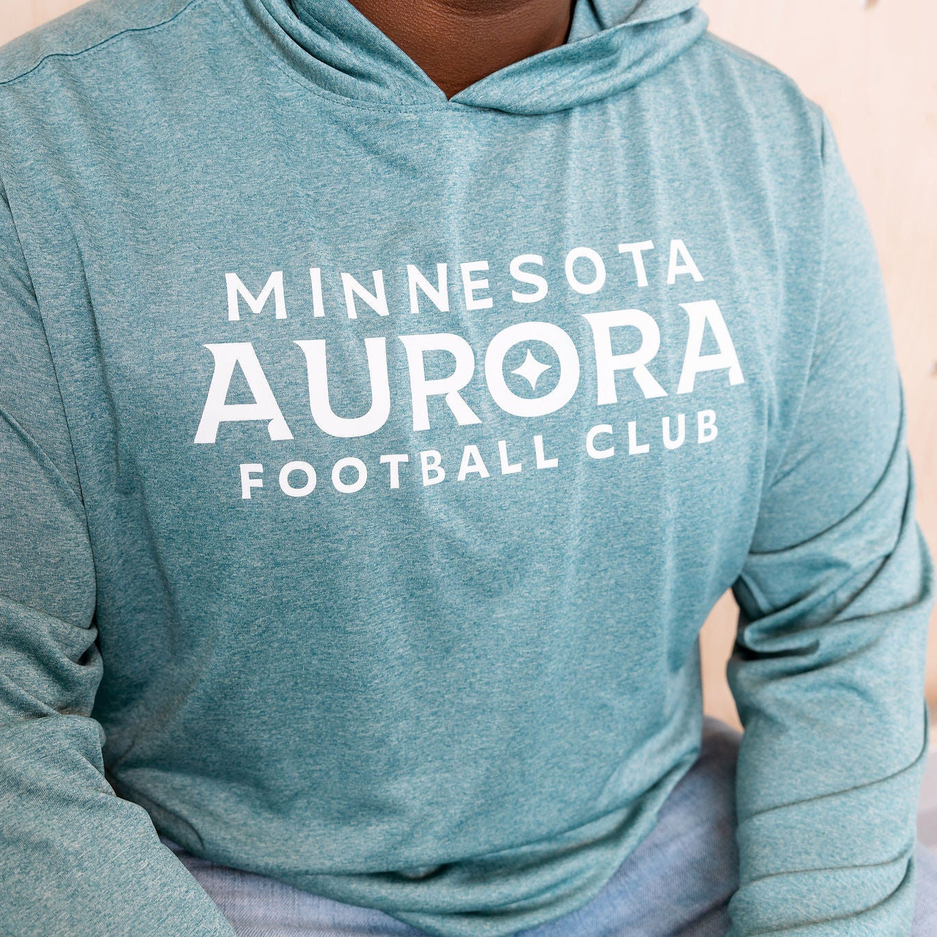 Person wearing a teal hoodie with 'Minnesota Aurora Football Club' text.
