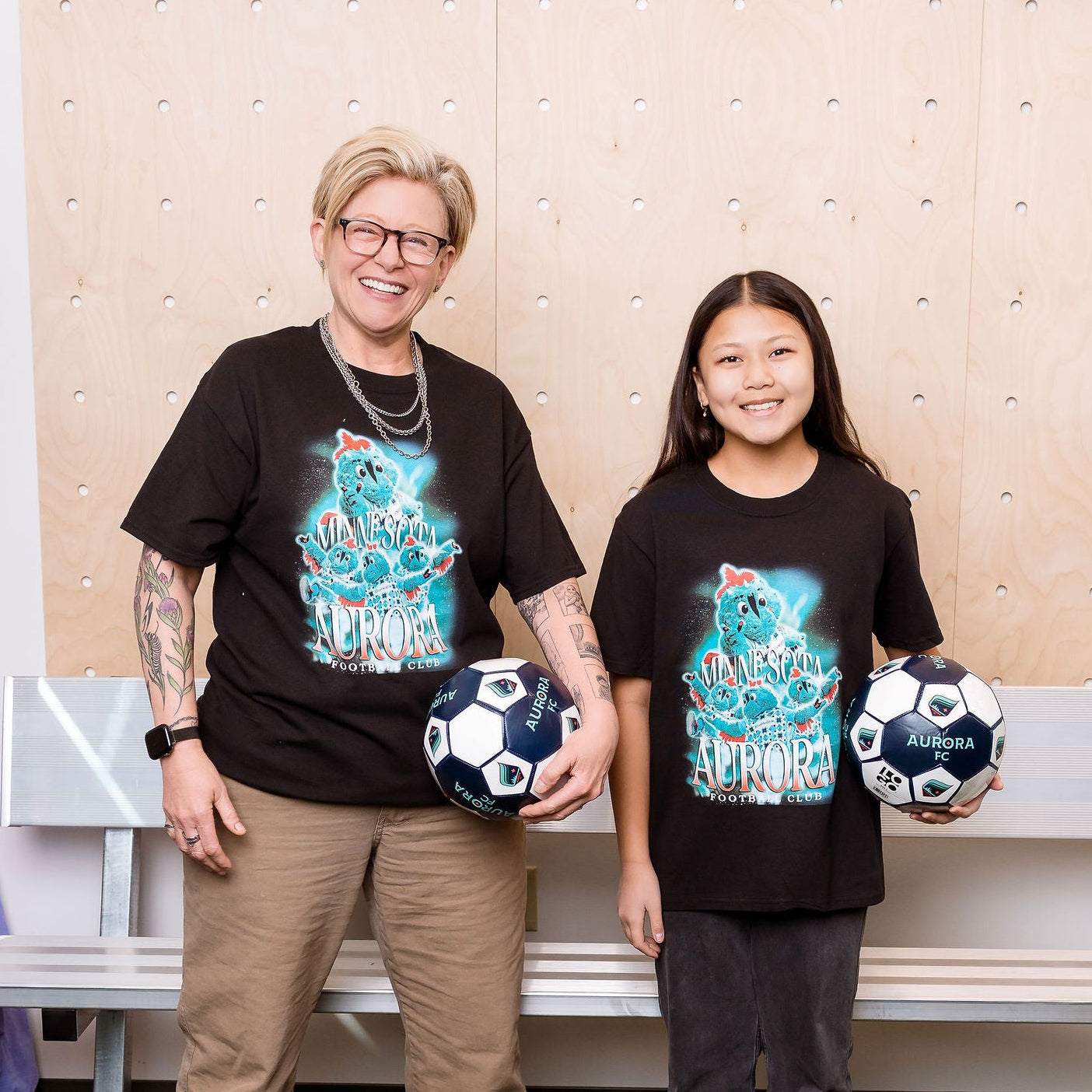 Two people standing in matching shirts holding soccer balls.